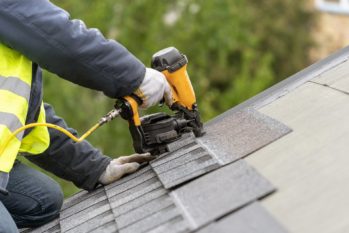 Roofer using a pneumatic nail gun to install shingles on a roof.