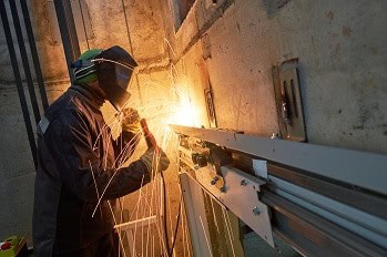 Elevator repairman welding on mechanical equipment in an elevator shaft.